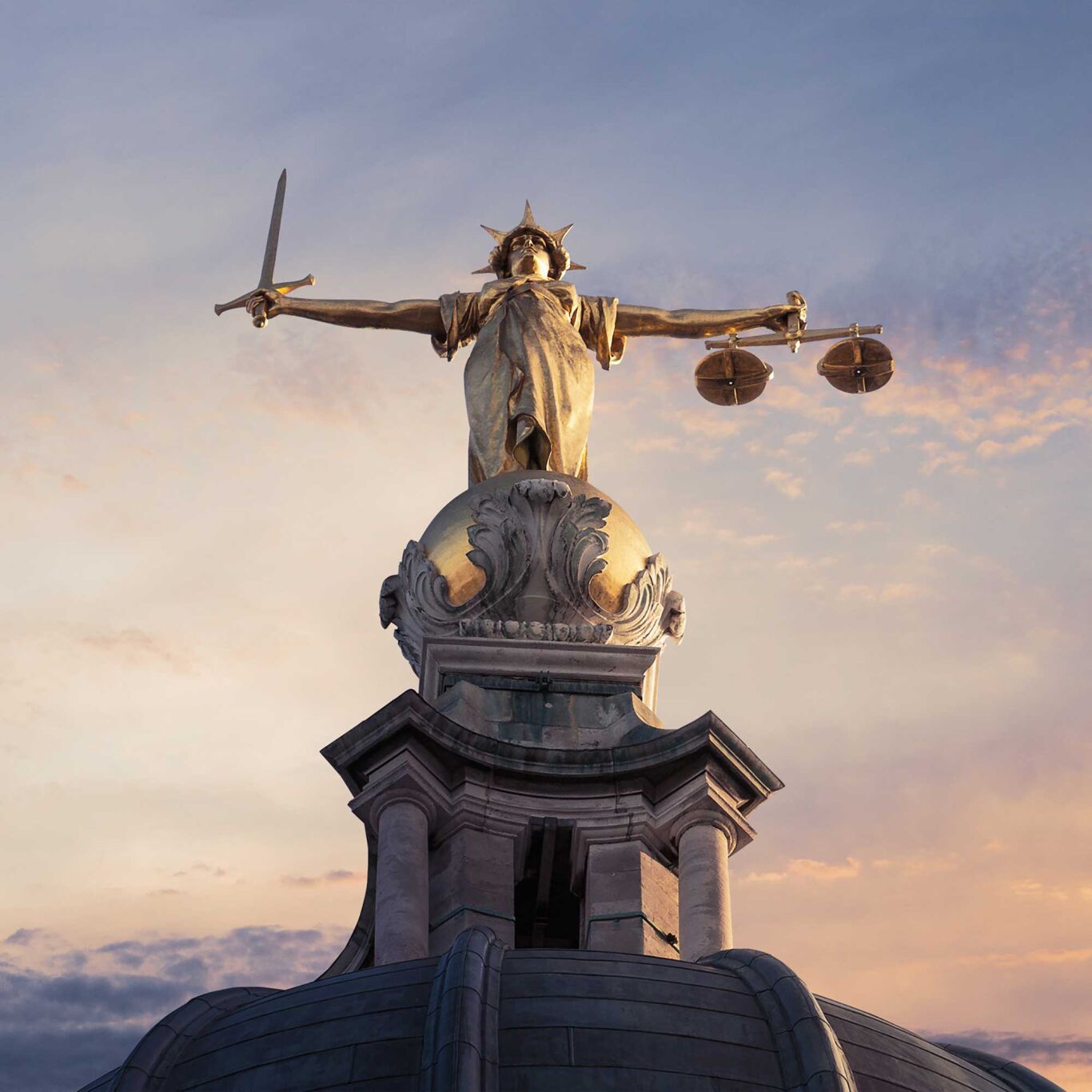 Large statue of lady justice with sunset background.
